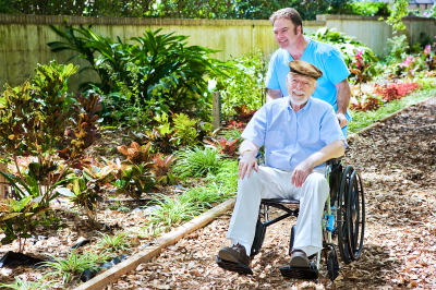 disabled senior man being pushed through a lovely garden by his nurse